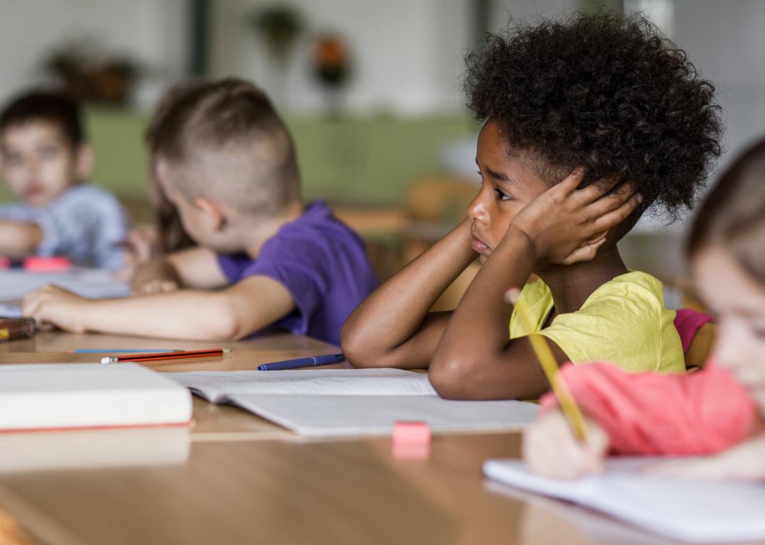 Child in school covering ears looking worried and upset struggling to work or study.