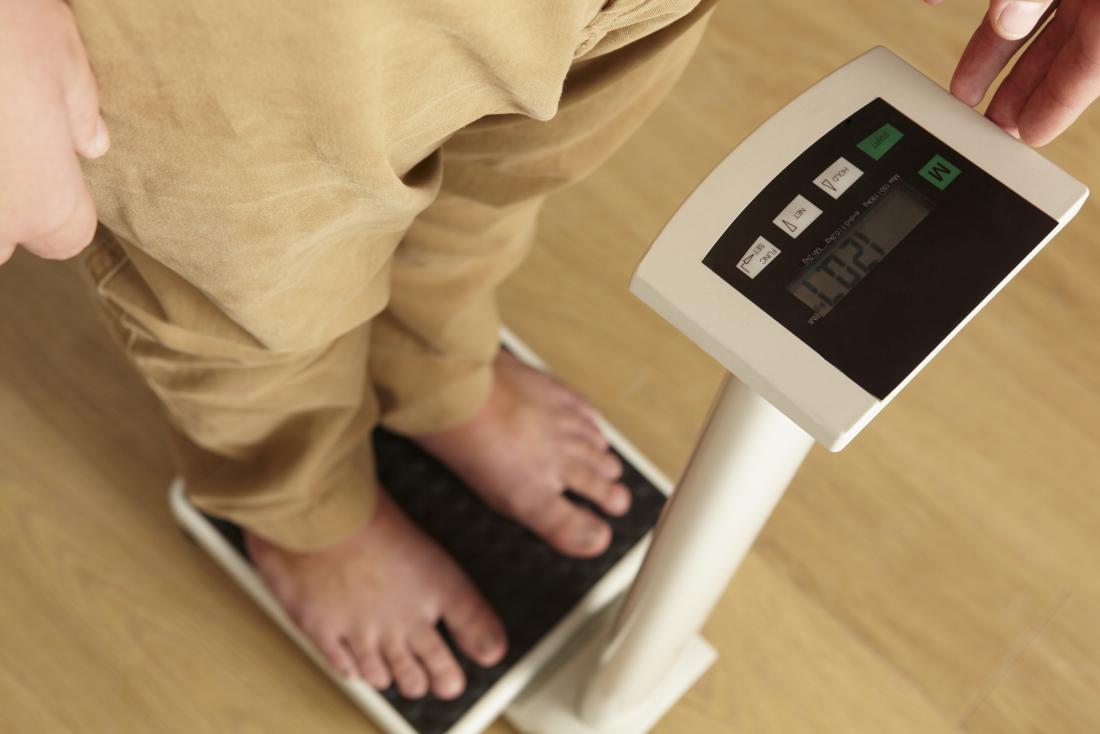 Man experiencing unexplained weight loss alo<em></em>ngside heartburn and nausea stands on scales.