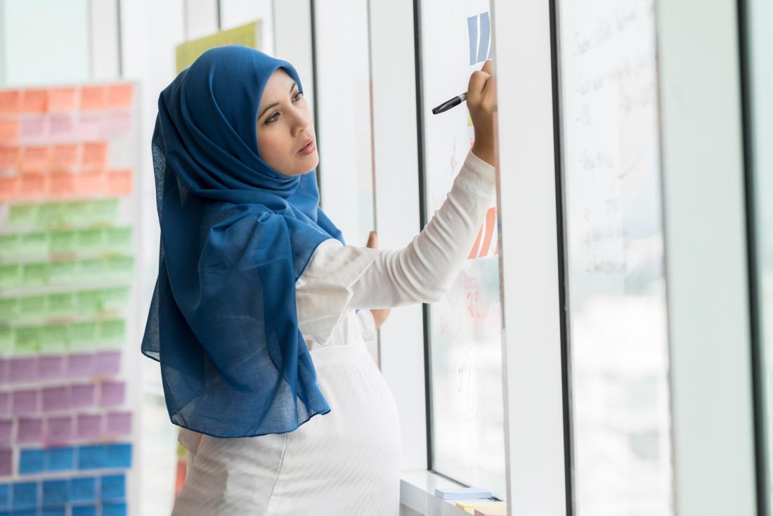 Pregnant woman with heartburn and nausea writes on sticky notes on window in office.