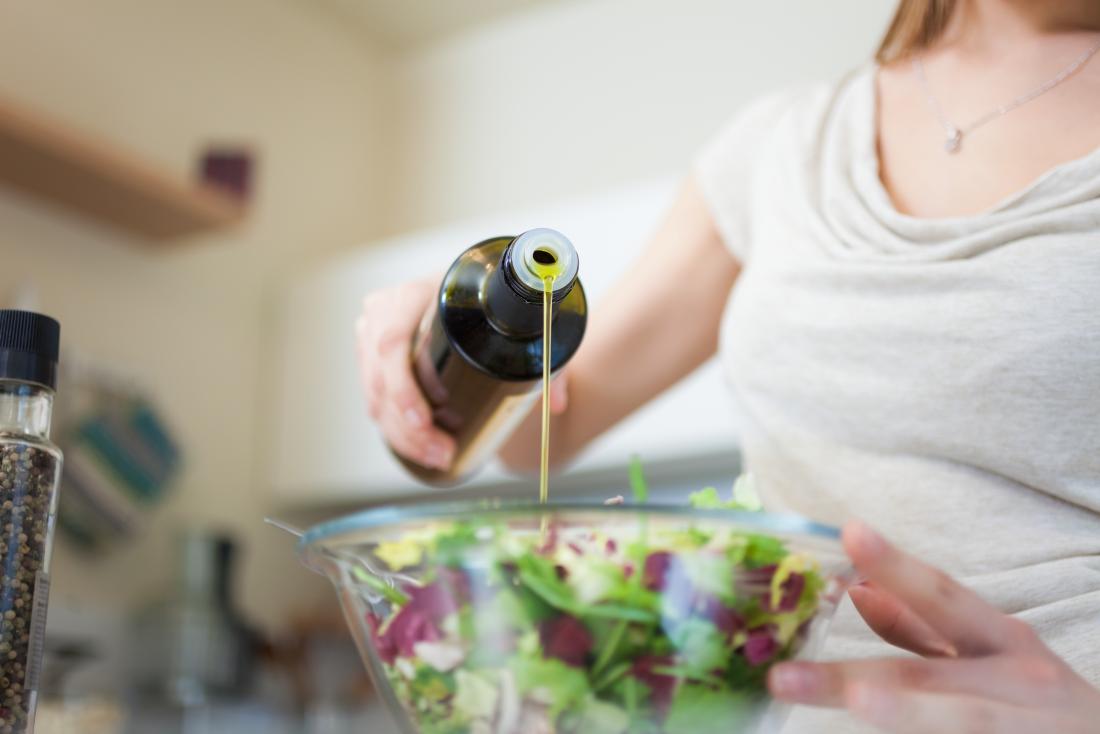 Woman pouring olive oil o<em></em>nto salad