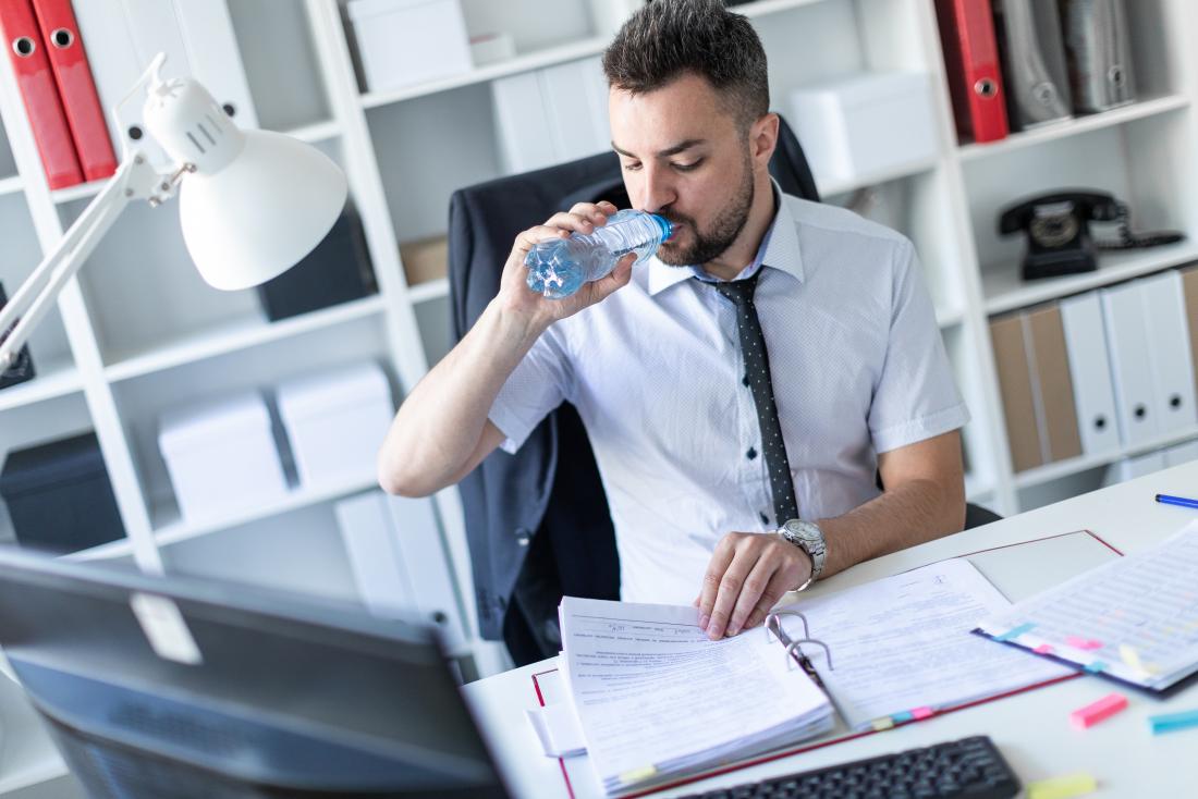 young man at work desk drinking bottle of water
