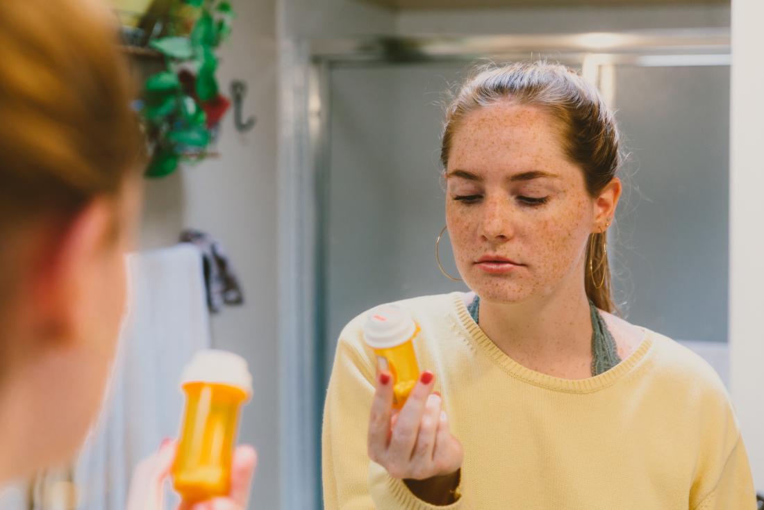 young woman reading label on co<em></em>ntainer of mood stabilizers 