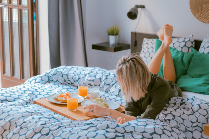 A woman with a room service tray on a hotel bed