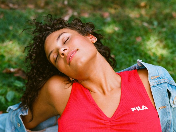 woman in a denim jacker and sports bra stretching in the shade, on grass