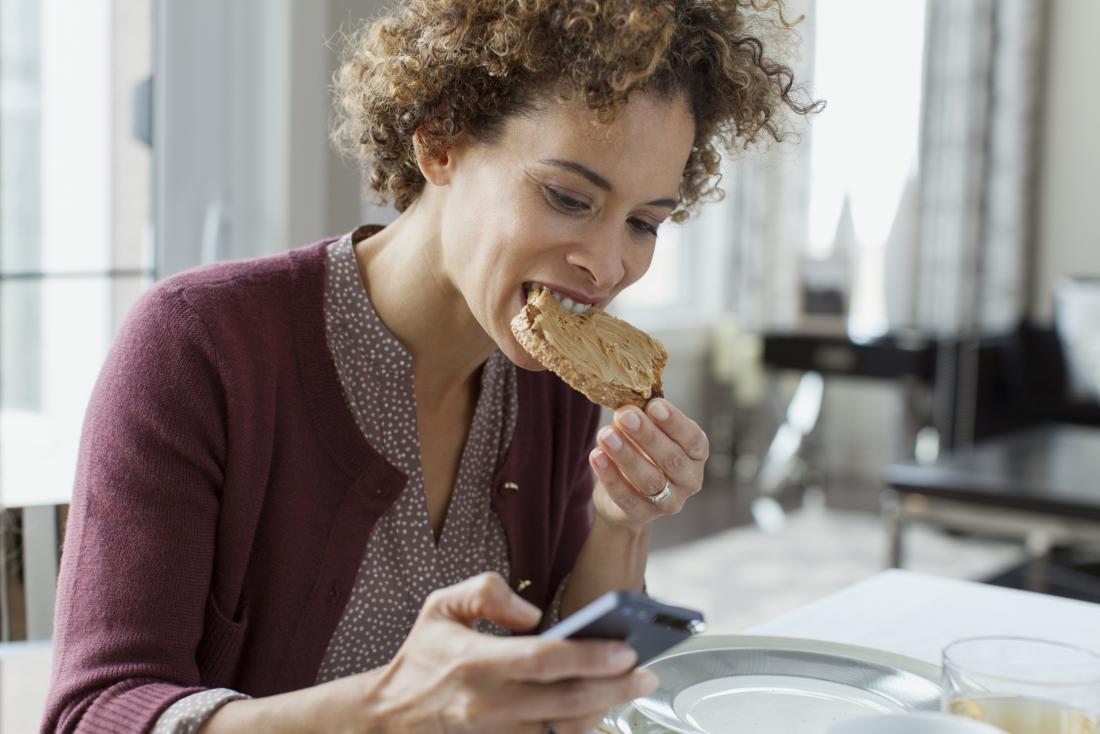 woman eating toast while looking at mobile phone