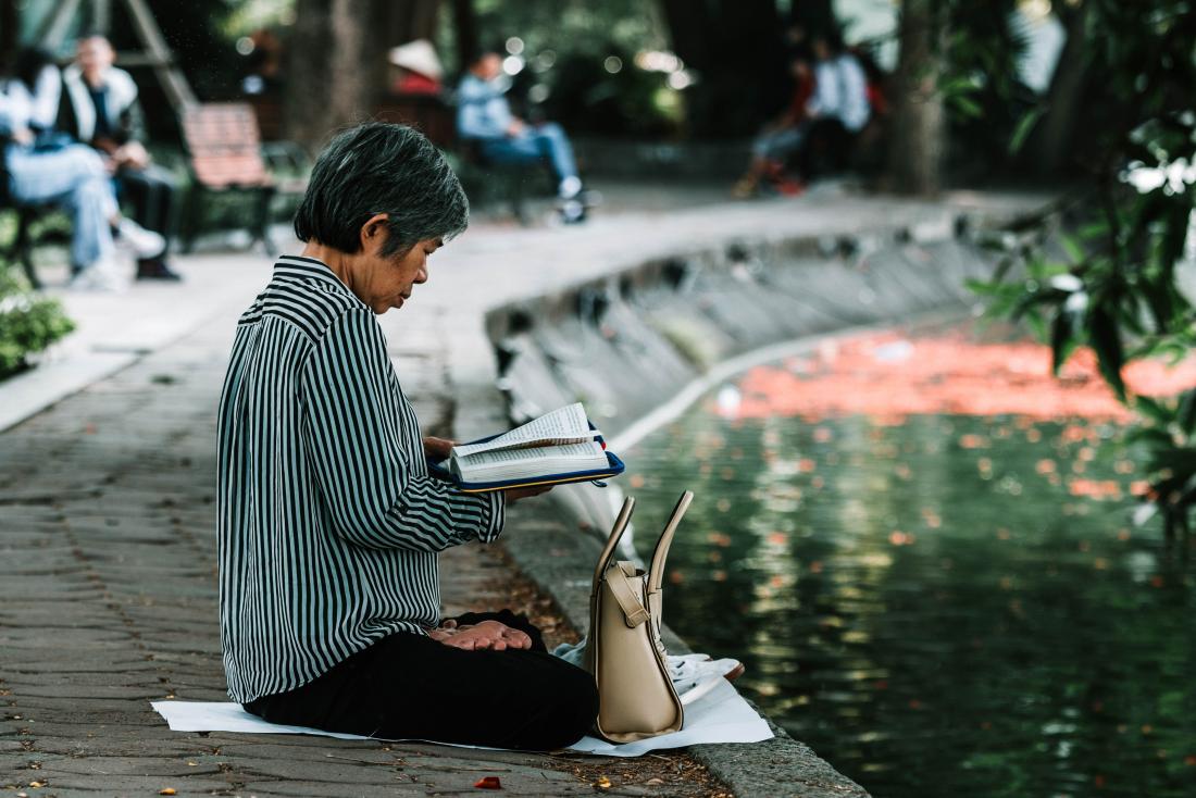 older person sitting cross legged reading a book