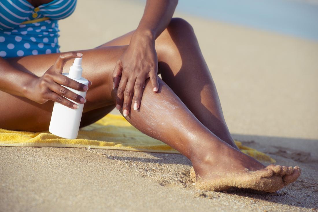 Person with black or brown skin sitting on beach applying sunscreen