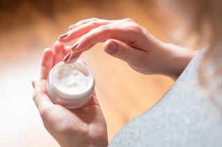 A woman holding a co<em></em>ntainer of skin cream.